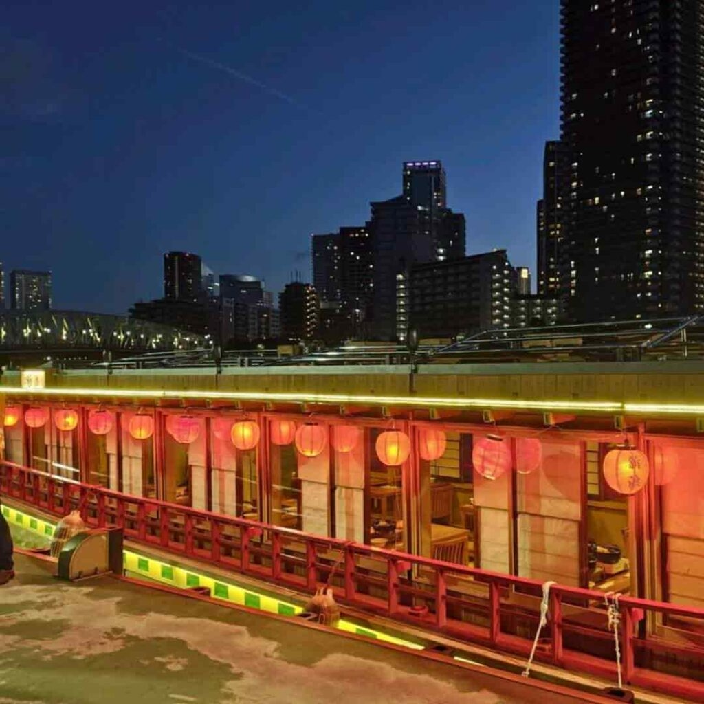 Yakatabune houseboat with red lanterns docked against the Tokyo skyline at dusk