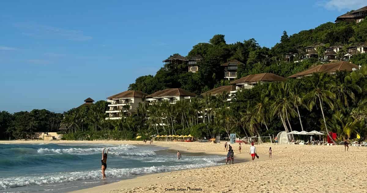 Boracay beach with white sand, turquoise waves, and hillside resorts in the Philippines
